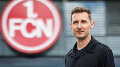 Der neue Trainer Miroslav Klose steht vor dem Vereins-Logo des 1. FC Nürnberg