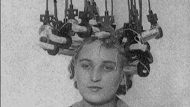 Schwarz-Weiß-Aufnahme einer Frau mit Wicklern und Haube beim Friseur