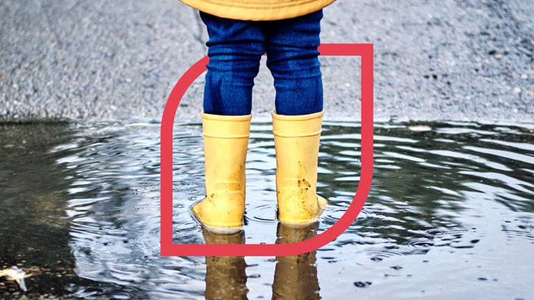 Ein Kind mit gelben Gummistiefel steht in einer Pfütze