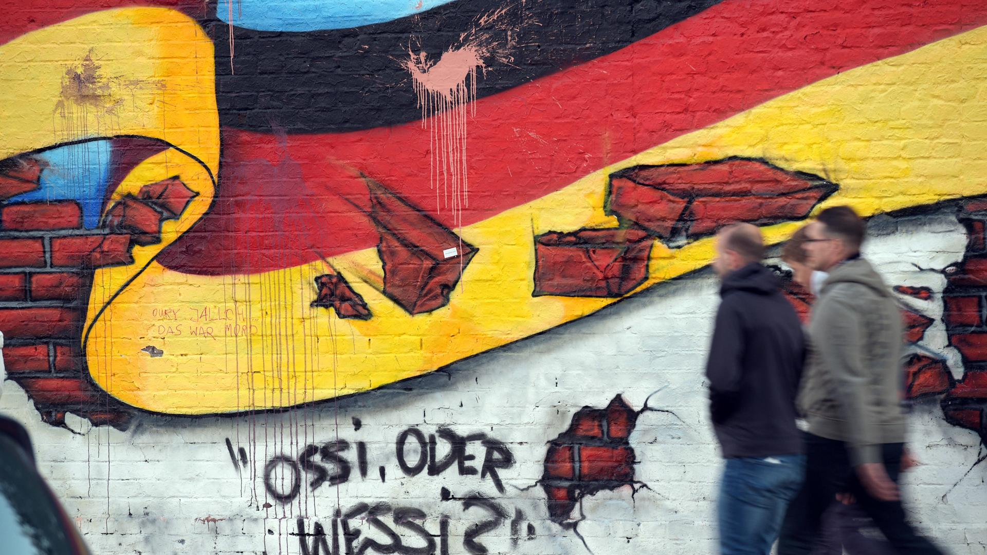 Passanten gehen am 02.10.2015 in Berlin an an einem Wandbild mit der deutschen Nationalflagge und dem Schriftzug "Ossi oder Wessi? vorbei. 