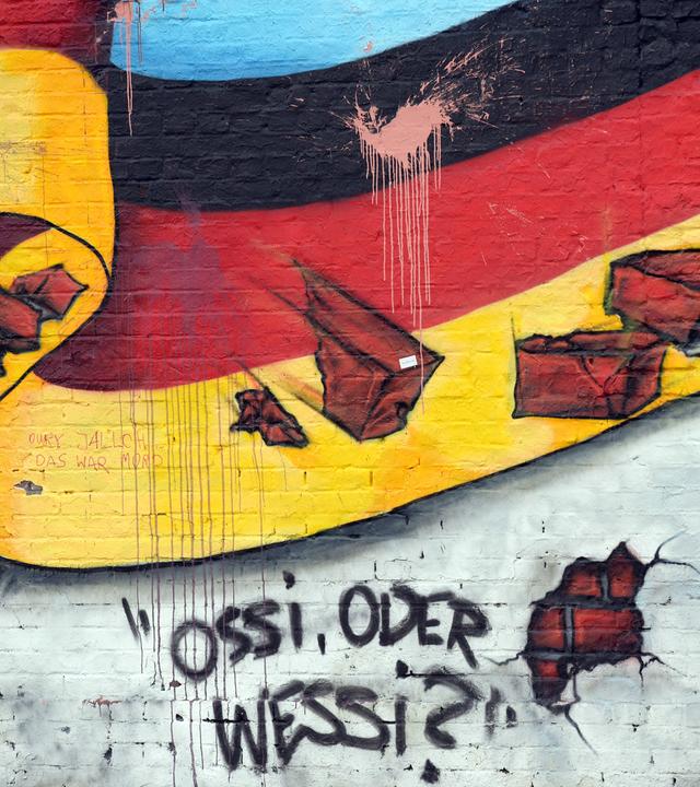Passanten gehen am 02.10.2015 in Berlin an an einem Wandbild mit der deutschen Nationalflagge und dem Schriftzug "Ossi oder Wessi? vorbei. 