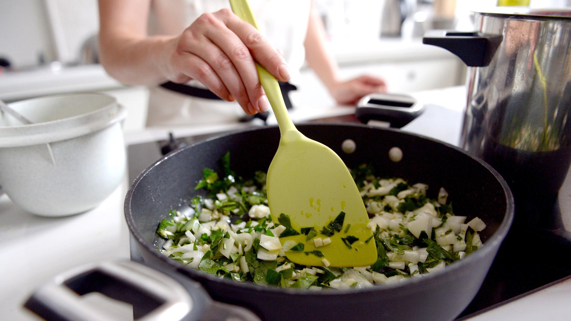 Frau steht zu Hause am Herd und rührt in Pfanne mit Gemüse