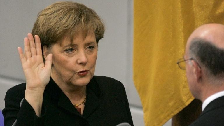 Merkel erhebt die Hand und spricht etwas dabei.