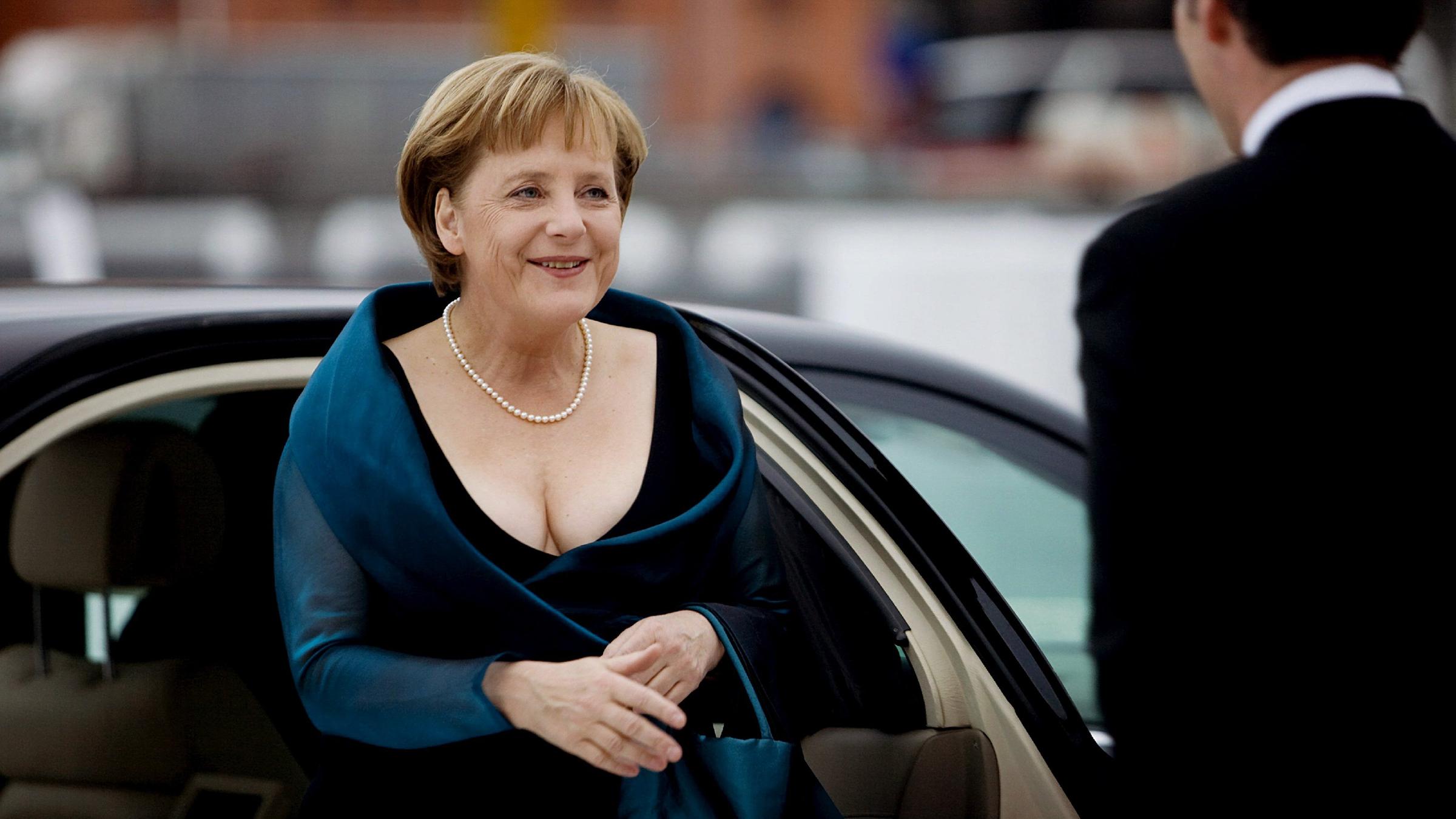 Angela Merkel ist in einem Kleid mit Perlenkette und Handtasche zu sehen. 