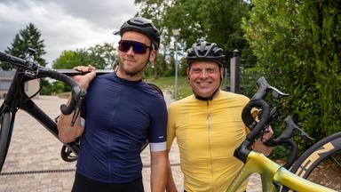 "Terra Xplore: Jan Ullrich: Hochleistung trotz Depression?": Leon Windscheid (links) und dem ehemaligen Radrenn-Profi Jan Ullrich (rechts) posieren für die Kamera. Beide haben ihr Fahrrad in der Hand und haben den Blick in die Kamera gerichtet. Leon trägt eine Sonnenbrille.