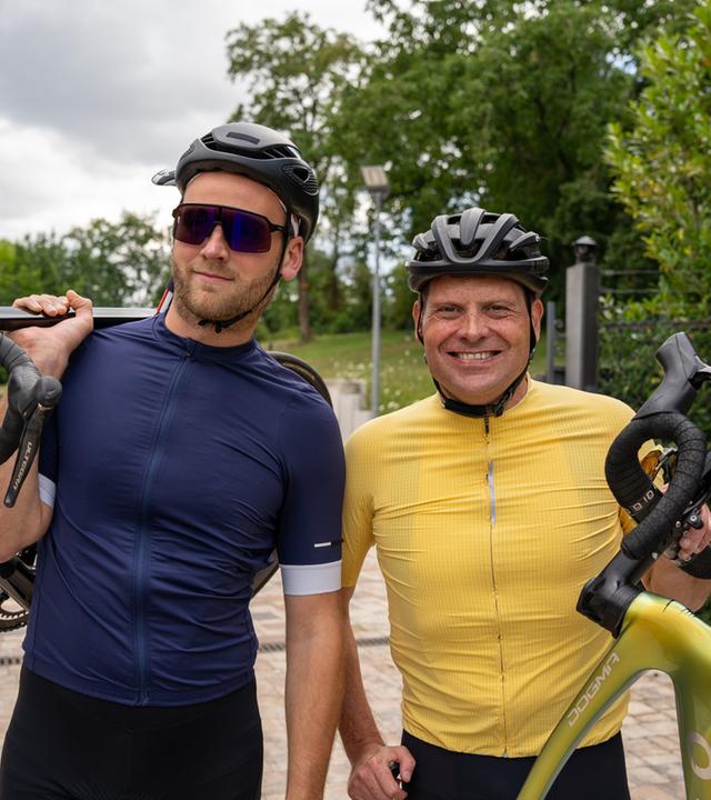 "Terra Xplore: Jan Ullrich: Hochleistung trotz Depression?": Leon Windscheid (links) und dem ehemaligen Radrenn-Profi Jan Ullrich (rechts) posieren für die Kamera. Beide haben ihr Fahrrad in der Hand und haben den Blick in die Kamera gerichtet. Leon trägt eine Sonnenbrille.