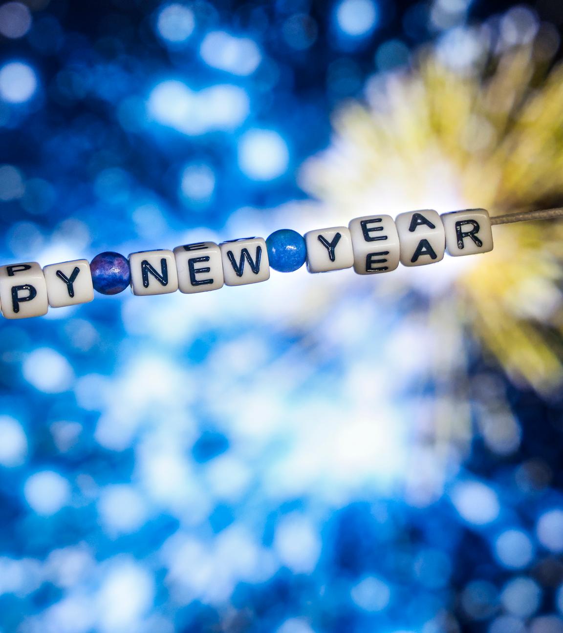 Der Schriftzug "Happy New Year" (Frohes Neues Jahr) aus Buchstabenwürfeln hängt vor dem Foto eines Feuerwerks auf einem Computerbildschirm. 