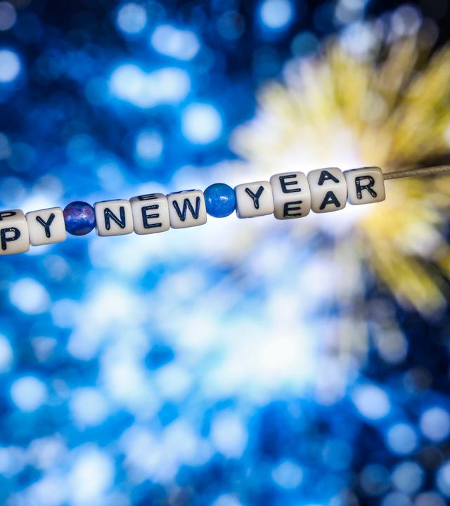 Der Schriftzug "Happy New Year" (Frohes Neues Jahr) aus Buchstabenwürfeln hängt vor dem Foto eines Feuerwerks auf einem Computerbildschirm. 