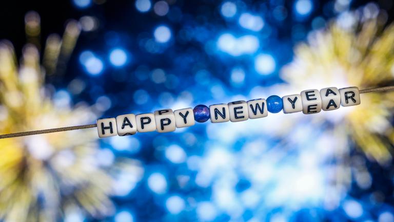 Der Schriftzug "Happy New Year" (Frohes Neues Jahr) aus Buchstabenwürfeln hängt vor dem Foto eines Feuerwerks auf einem Computerbildschirm. 
