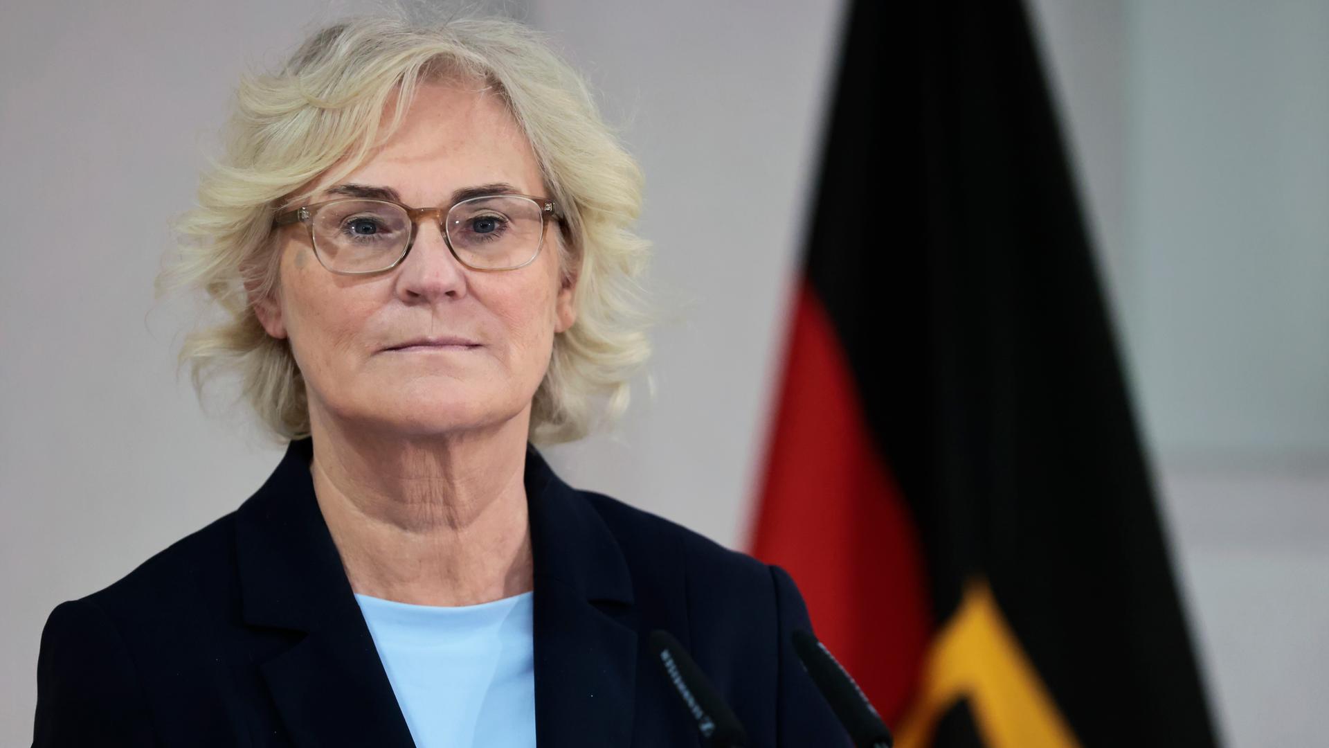 26.01.2022, Berlin: Christine Lambrecht steht vor einem Mikro und schaut in die Ferne. Im Hintergrund ist ein wenig der Deutschlandflagge zu sehen.