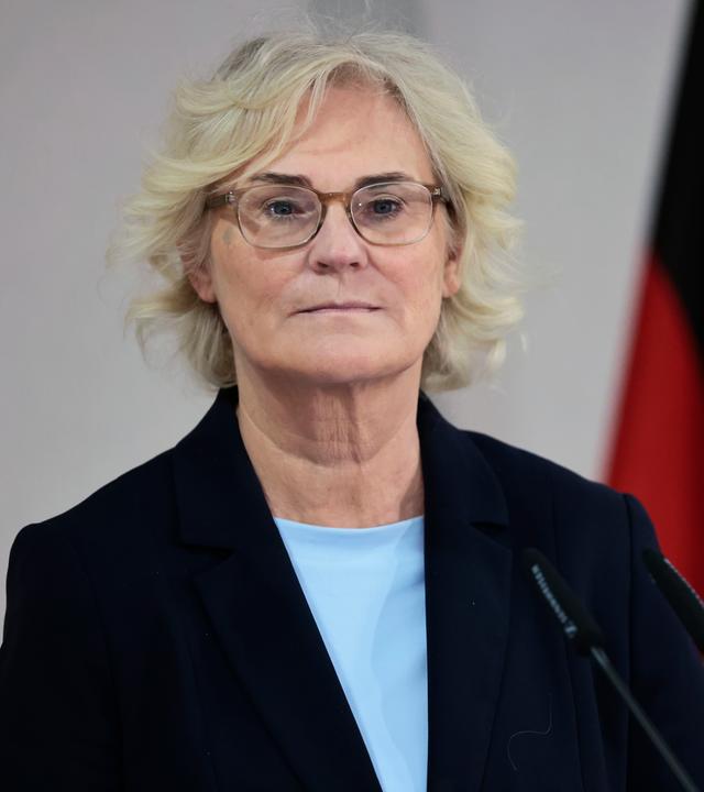 26.01.2022, Berlin: Christine Lambrecht steht vor einem Mikro und schaut in die Ferne. Im Hintergrund ist ein wenig der Deutschlandflagge zu sehen.