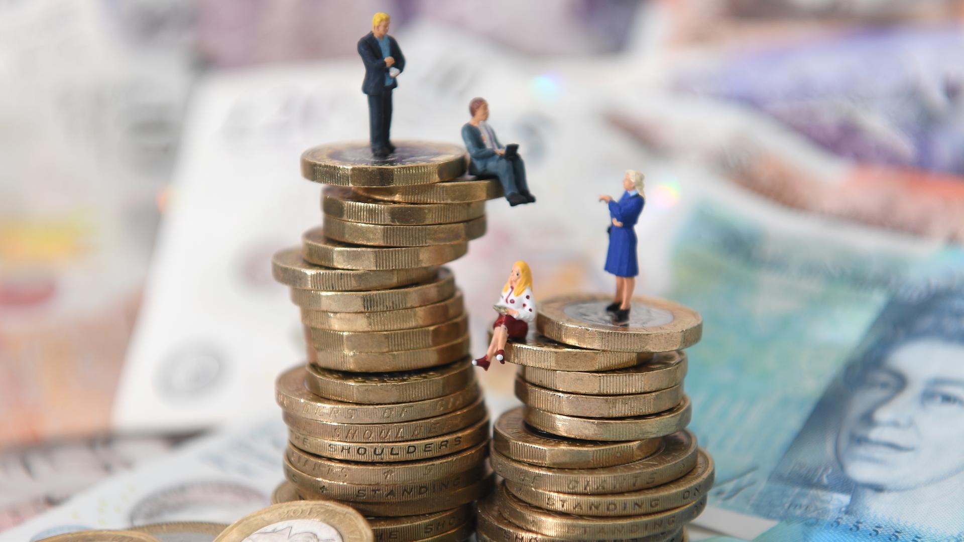 Kleine Figuren von Männern und Frauen sitzen auf Geldmünzen, um zu verdeutlichen, dass Frauen weniger verdienen als Männer