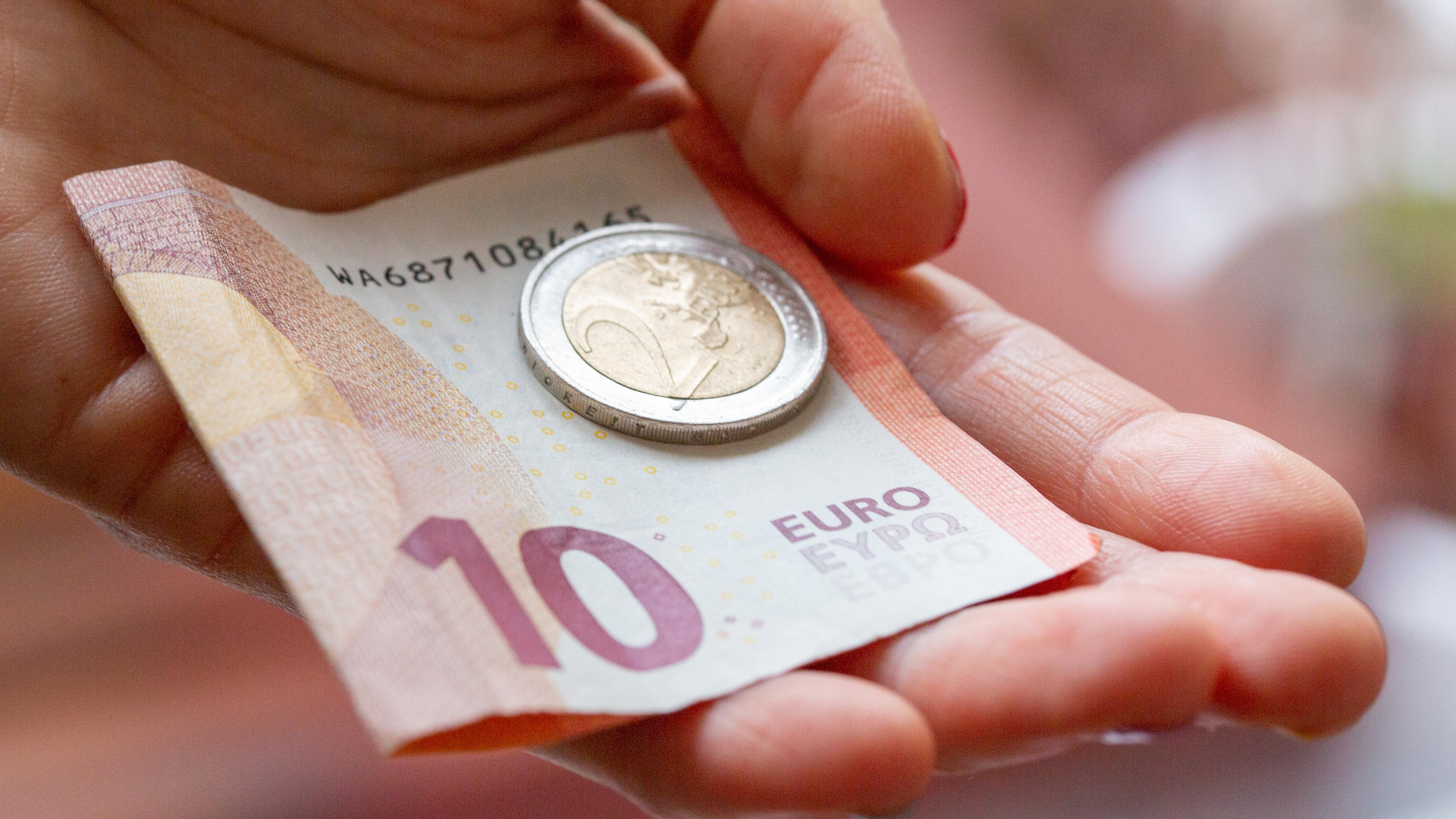 Ein 10 Euro-Schein und eine 2 Euro-Münze werden in die Kamera gezeigt, 10.02.2022, Symbolbild.