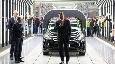 Grünheide bei Berlin, Deutschland, 22.03.2022: Tesla CEO Elon Musk spricht während der Eröffnung der Tesla "Gigafactory" vor einem Tesla auf einem großen Rollband. Bundeskanzler Scholz steht daneben