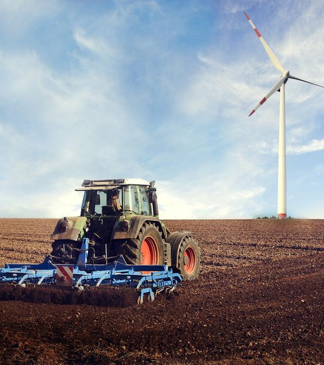 Traktor fährt auf eine Feld, im HIntergrund ein WIndrad