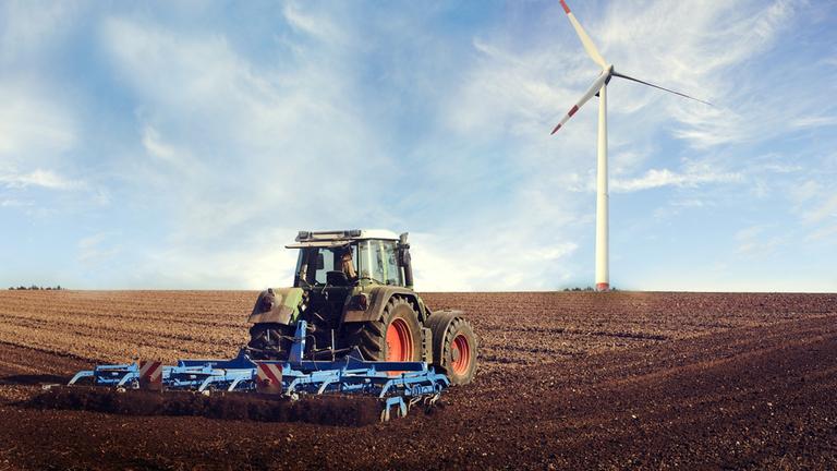 Traktor fährt auf eine Feld, im HIntergrund ein WIndrad
