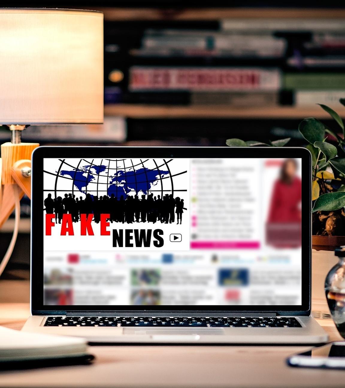 Laptop auf einem Schreibtisch. Zu sehen auf die  Bildschirm die Aufschrift "Fake News"