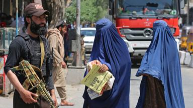 Afghanische mit Burka verschleierte Frauen laufen an einer Talibanwache vorbei