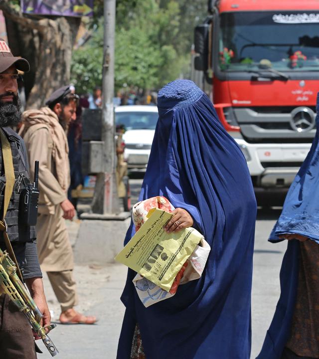 Afghanische mit Burka verschleierte Frauen laufen an einer Talibanwache vorbei