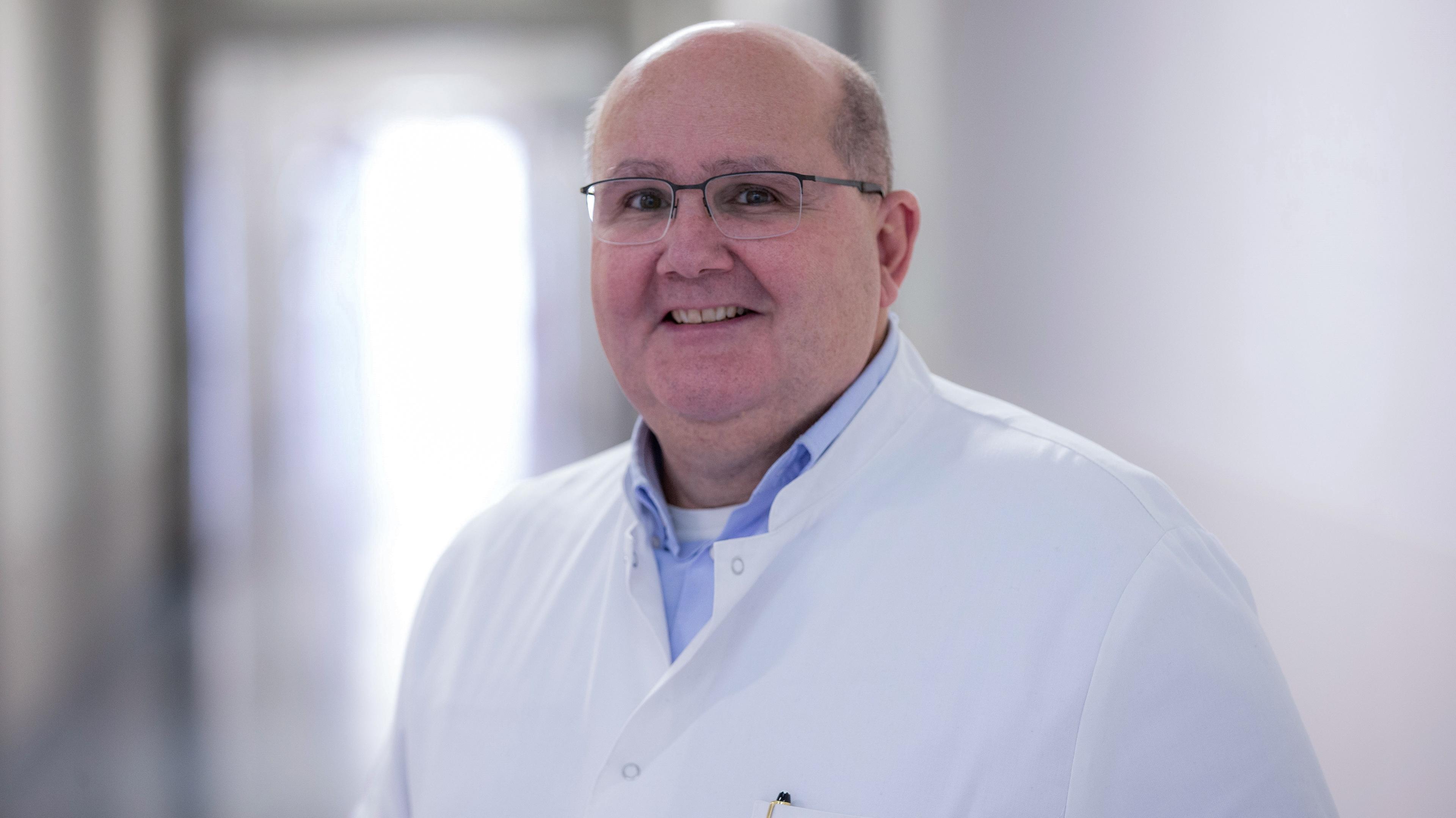 Prof. Dr. Bernhard Schieffer steht in einem Medizinerkittel in einem Krankenhausflur. Er trägt eine Brille und hat eine Halbglatze 