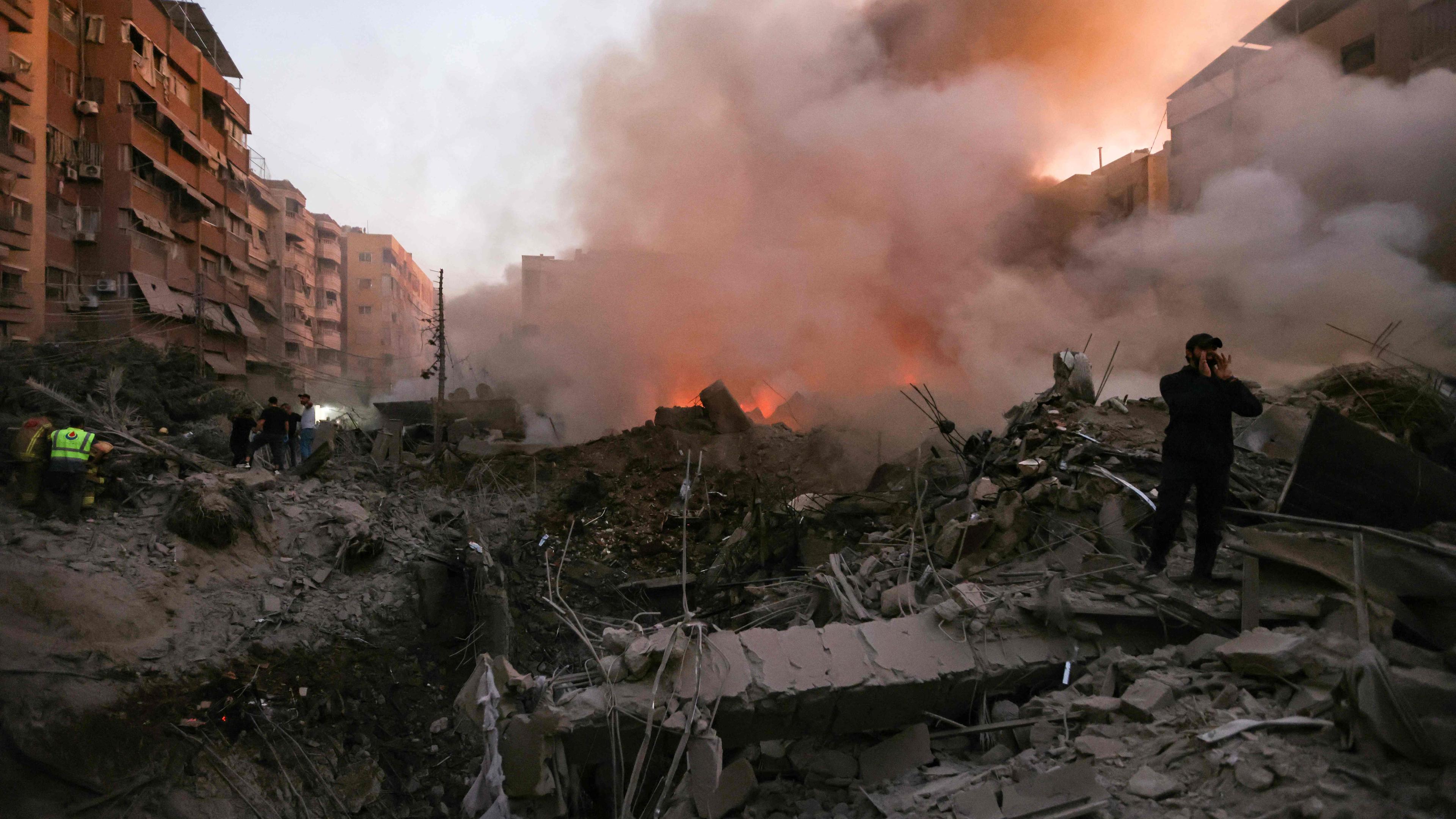 Menschen und Rettungskräfte versammeln sich am 27. September 2024 in der Nähe der schwelenden Trümmer eines durch einen israelischen Luftangriff zerstörten Gebäudes im Viertel Haret Hreik in den südlichen Vororten von Beirut. 