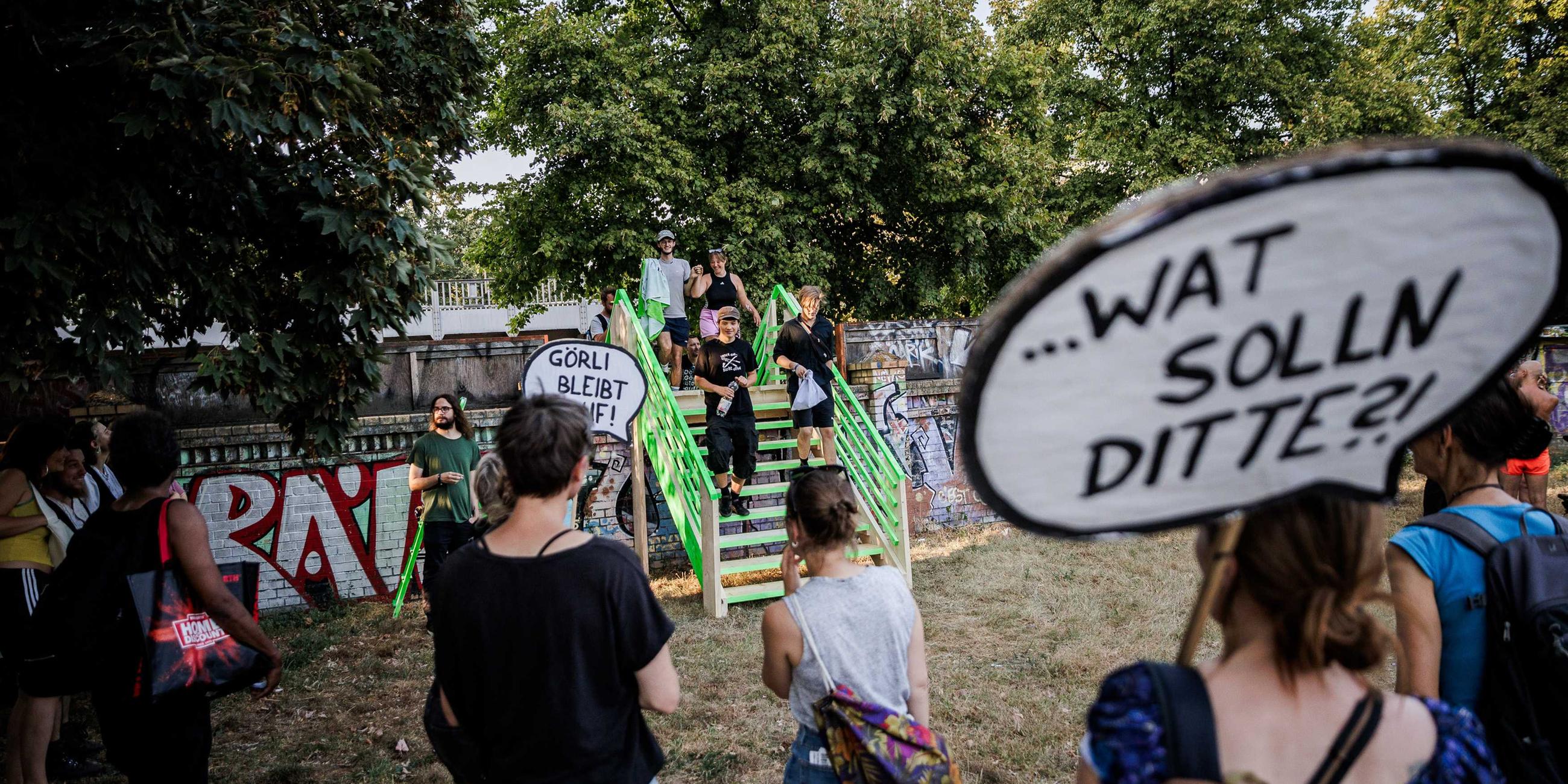 07.09.2024, Berlin: Teilnehmer einer Protestaktion in der in der Aktionswoche «Defence Görli» überqueren symbolisch eine provisorische Holztreppe über eine Mauer am Görlitzer Park als Protest gegen die geplante Umzäunung des Görlitzer Park.