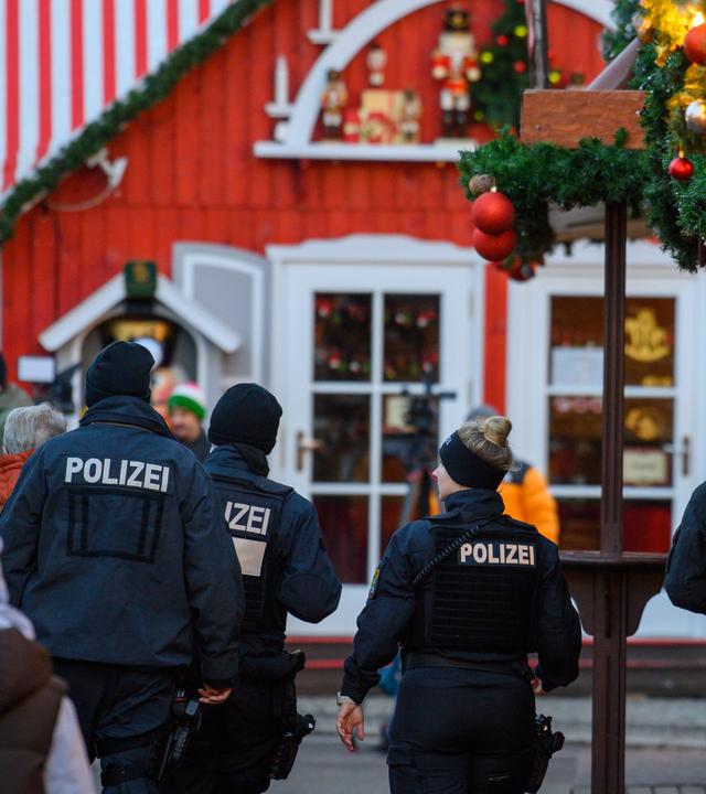  Polizisten und Passanten gehen über den geschlossenen Magdeburger Weihnachtsmarkt am 22.12.2024