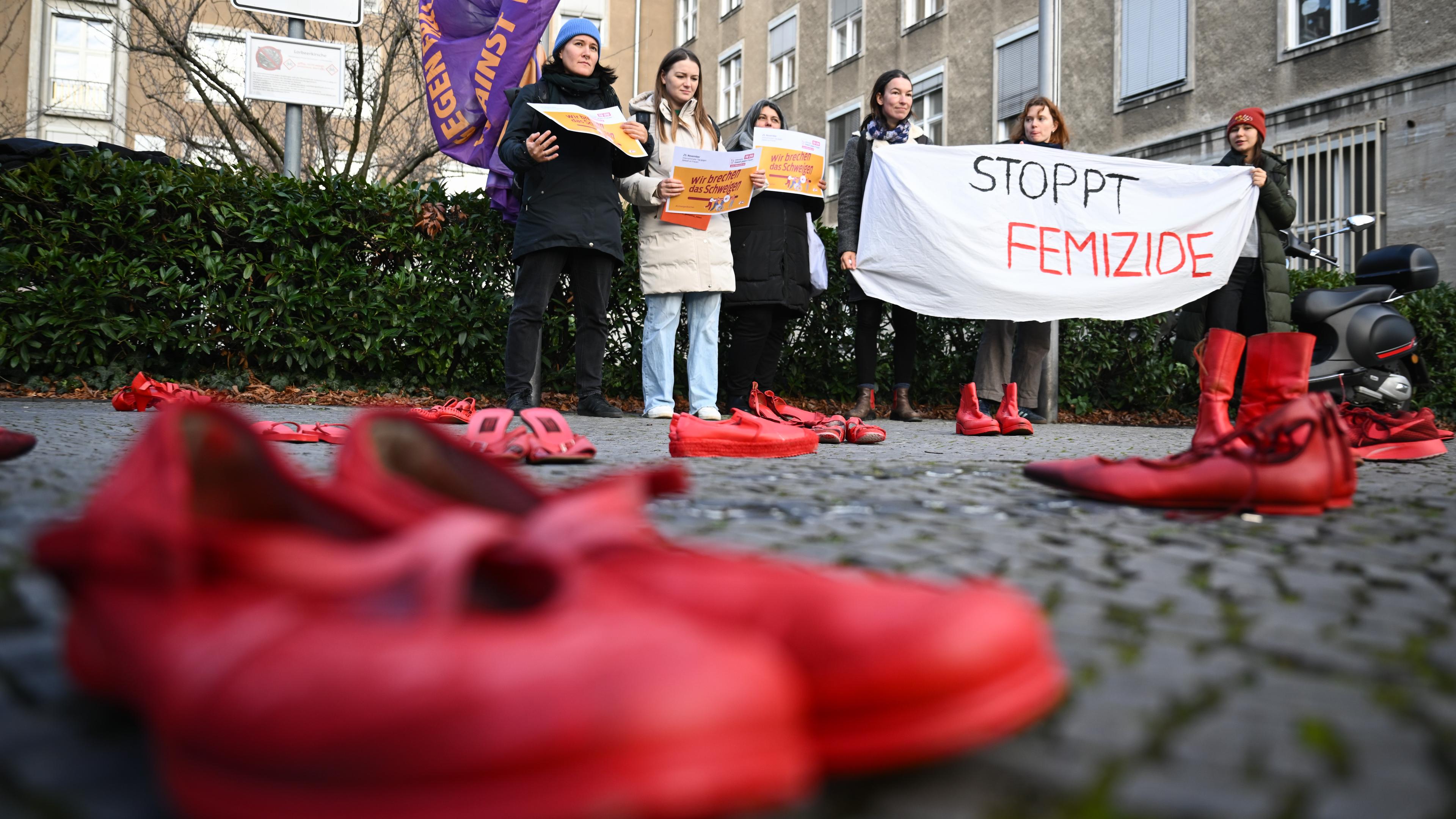 Teilnehmerinnen halten während des Hissens der Anti-Gewalt-Fahne anlässlich des Internationalen Tags für die Beseitigung von Gewalt gegen Frauen am Rathaus Tiergarten ein Banner mit der Aufschrift «Stoppt Femizide» hinter Roten Schuhen
