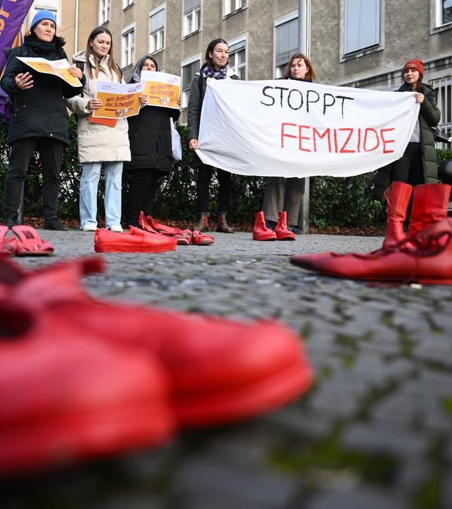 Teilnehmerinnen halten während des Hissens der Anti-Gewalt-Fahne anlässlich des Internationalen Tags für die Beseitigung von Gewalt gegen Frauen am Rathaus Tiergarten ein Banner mit der Aufschrift «Stoppt Femizide» hinter Roten Schuhen