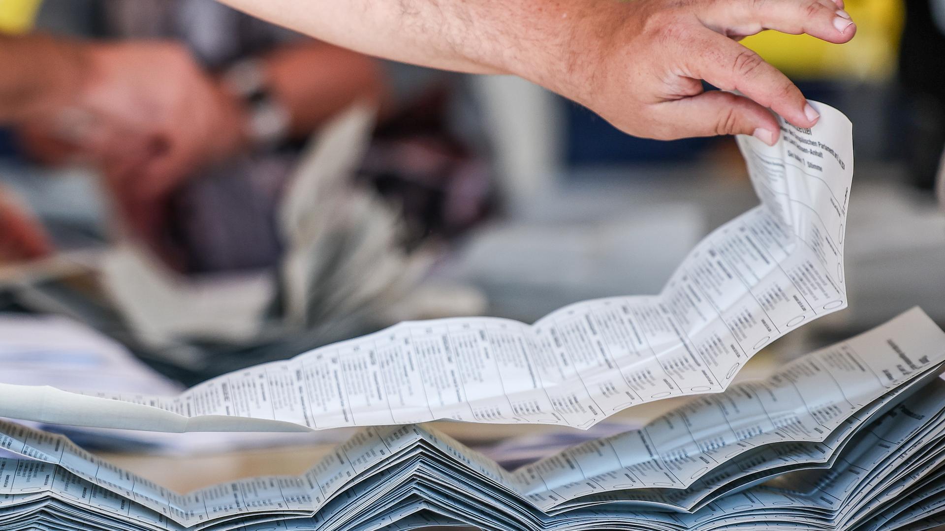 09.06.2024, Sachsen-Anhalt, Halle: Ein Wahlhelfer legt Stimmzettel zur Stimmenauszählung der Briefwahlstimmen zur Europawahl auf einem Stapel.