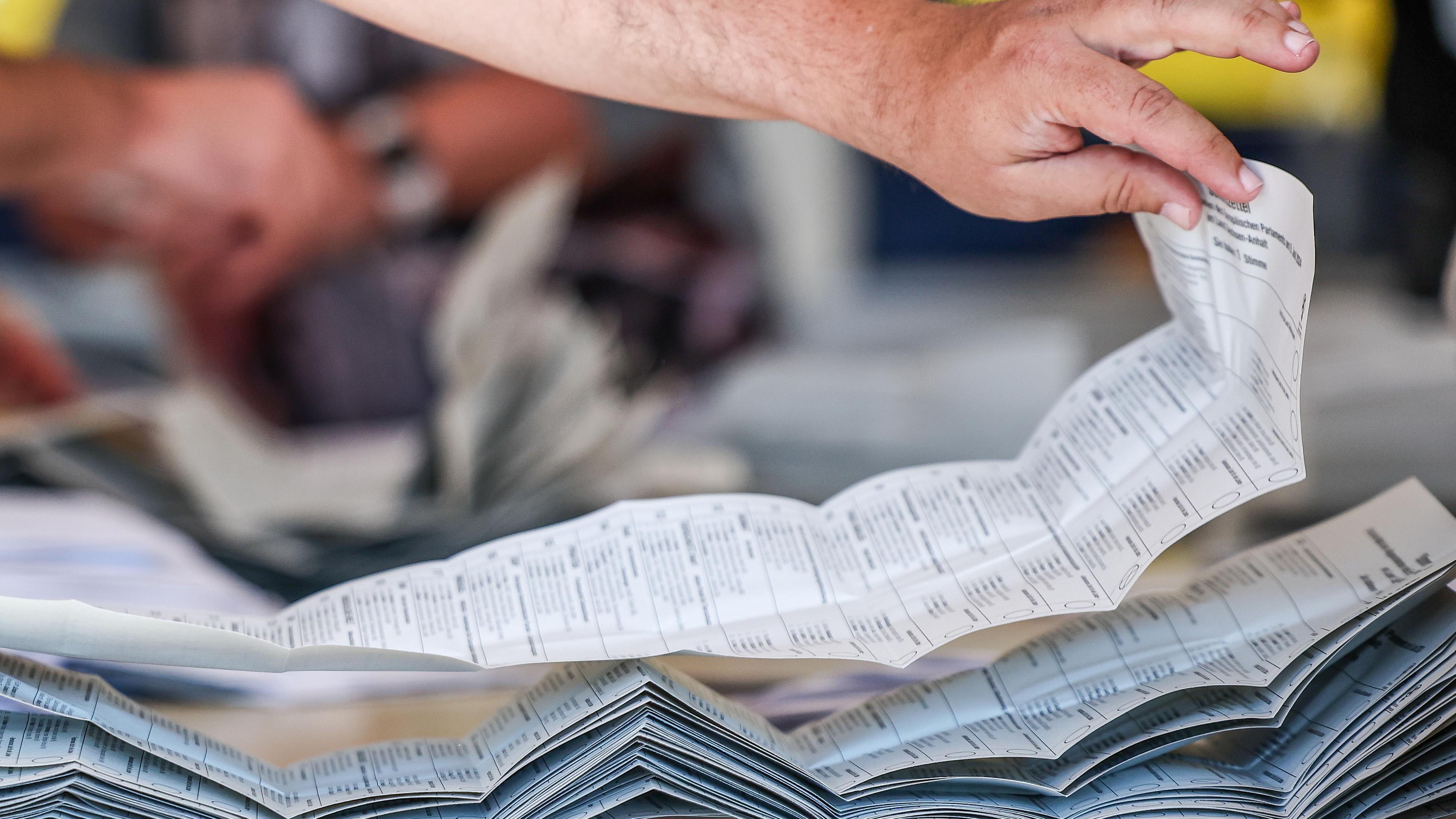 09.06.2024, Sachsen-Anhalt, Halle: Ein Wahlhelfer legt Stimmzettel zur Stimmenauszählung der Briefwahlstimmen zur Europawahl auf einem Stapel.