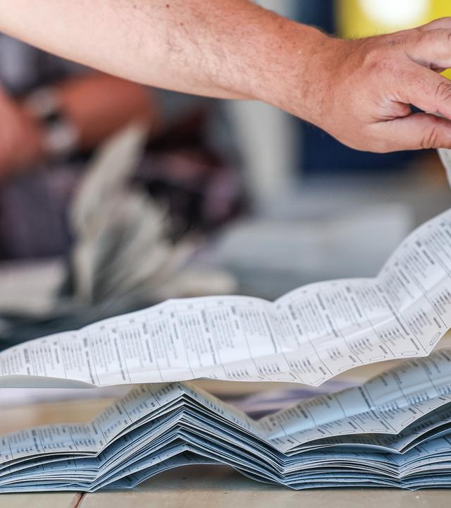 09.06.2024, Sachsen-Anhalt, Halle: Ein Wahlhelfer legt Stimmzettel zur Stimmenauszählung der Briefwahlstimmen zur Europawahl auf einem Stapel.