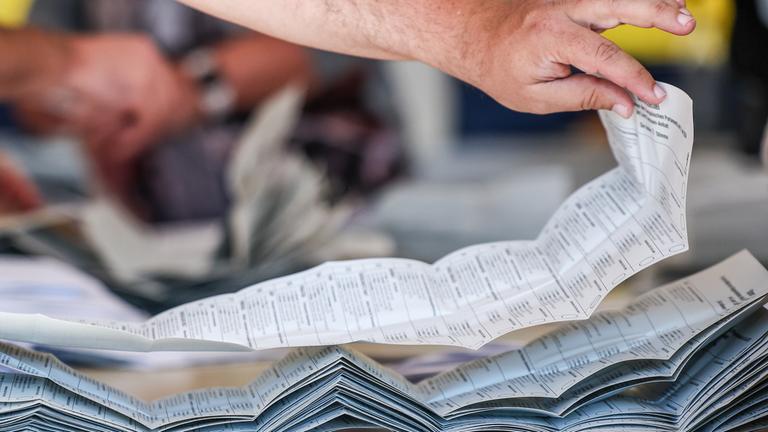 09.06.2024, Sachsen-Anhalt, Halle: Ein Wahlhelfer legt Stimmzettel zur Stimmenauszählung der Briefwahlstimmen zur Europawahl auf einem Stapel.
