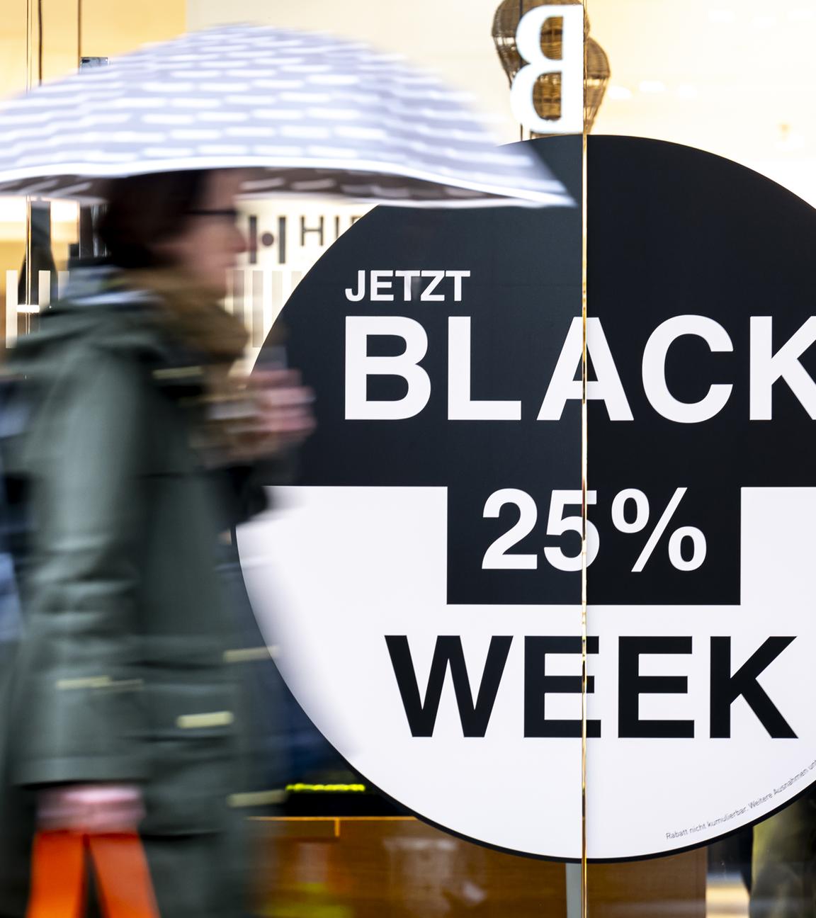 Schweiz, Bern: Eine Person mit einem Regenschirm geht an einem Geschäft vorbei, das für Angebote im Rahmen der Black Week wirbt.