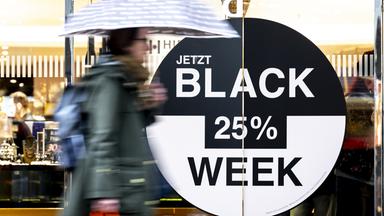 Schweiz, Bern: Eine Person mit einem Regenschirm geht an einem Geschäft vorbei, das für Angebote im Rahmen der Black Week wirbt.