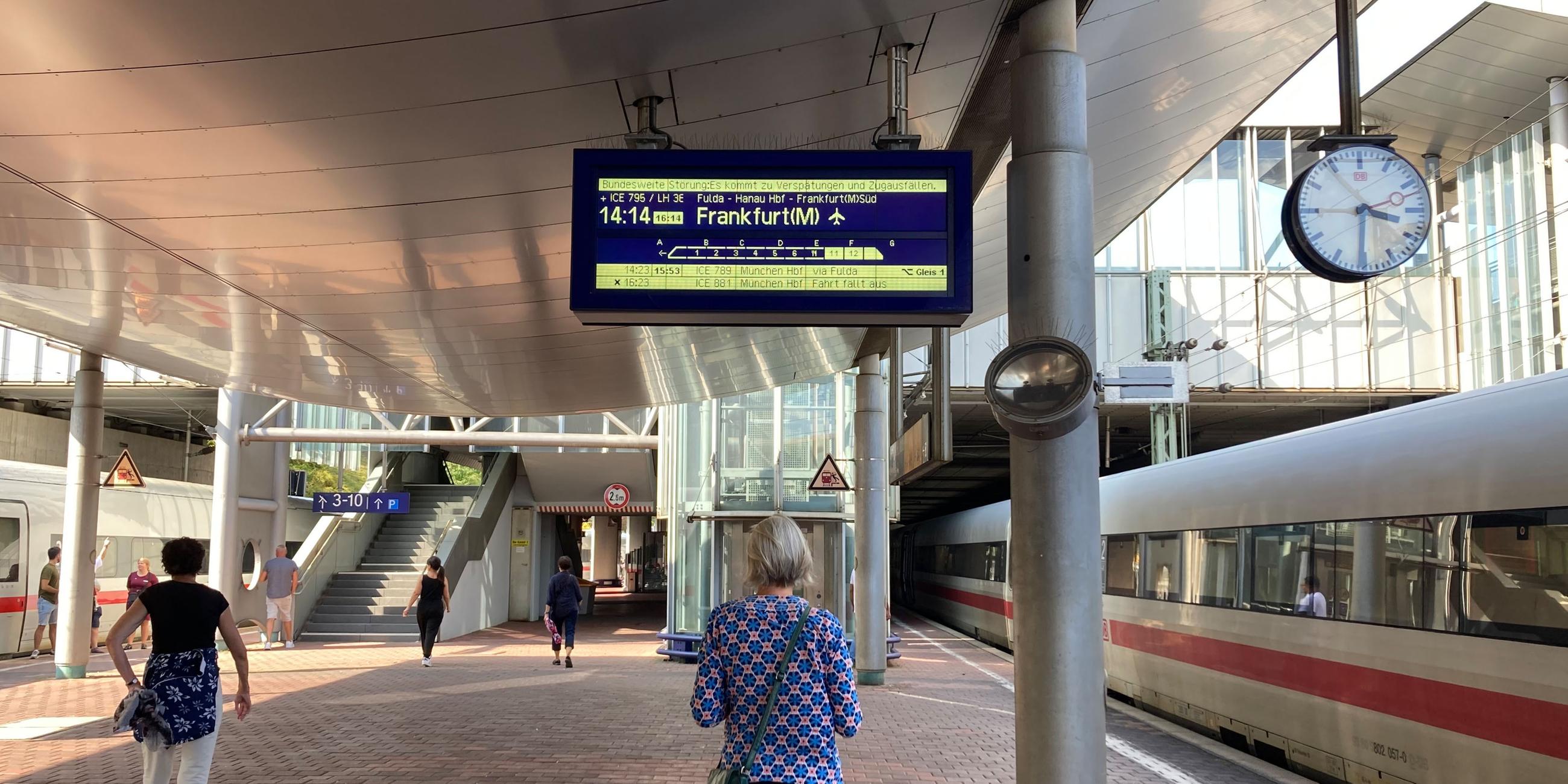 Ein Frau steht auf dem Bahnsteig und schaut sich eine Anzeige der Deutsche Bahn an.