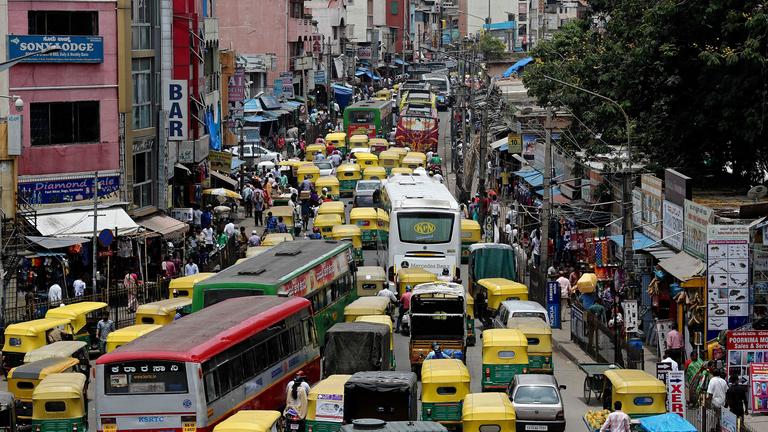 Auf dem Bild ist eine überfüllte Straße mit Rikschas und Taxis zu sehen.