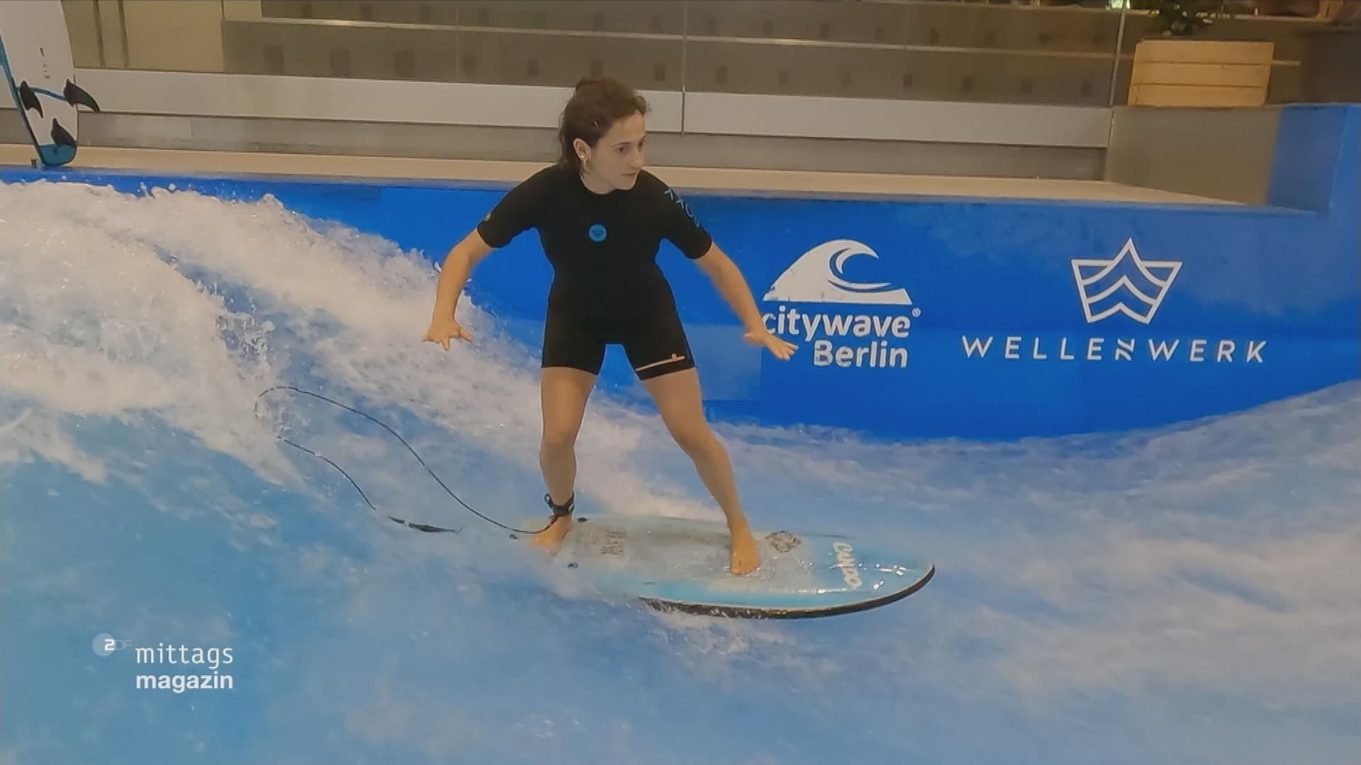 ZDF-Reporterin Saadet Czapski steht auf einem Surfbrett auf einer Welle 