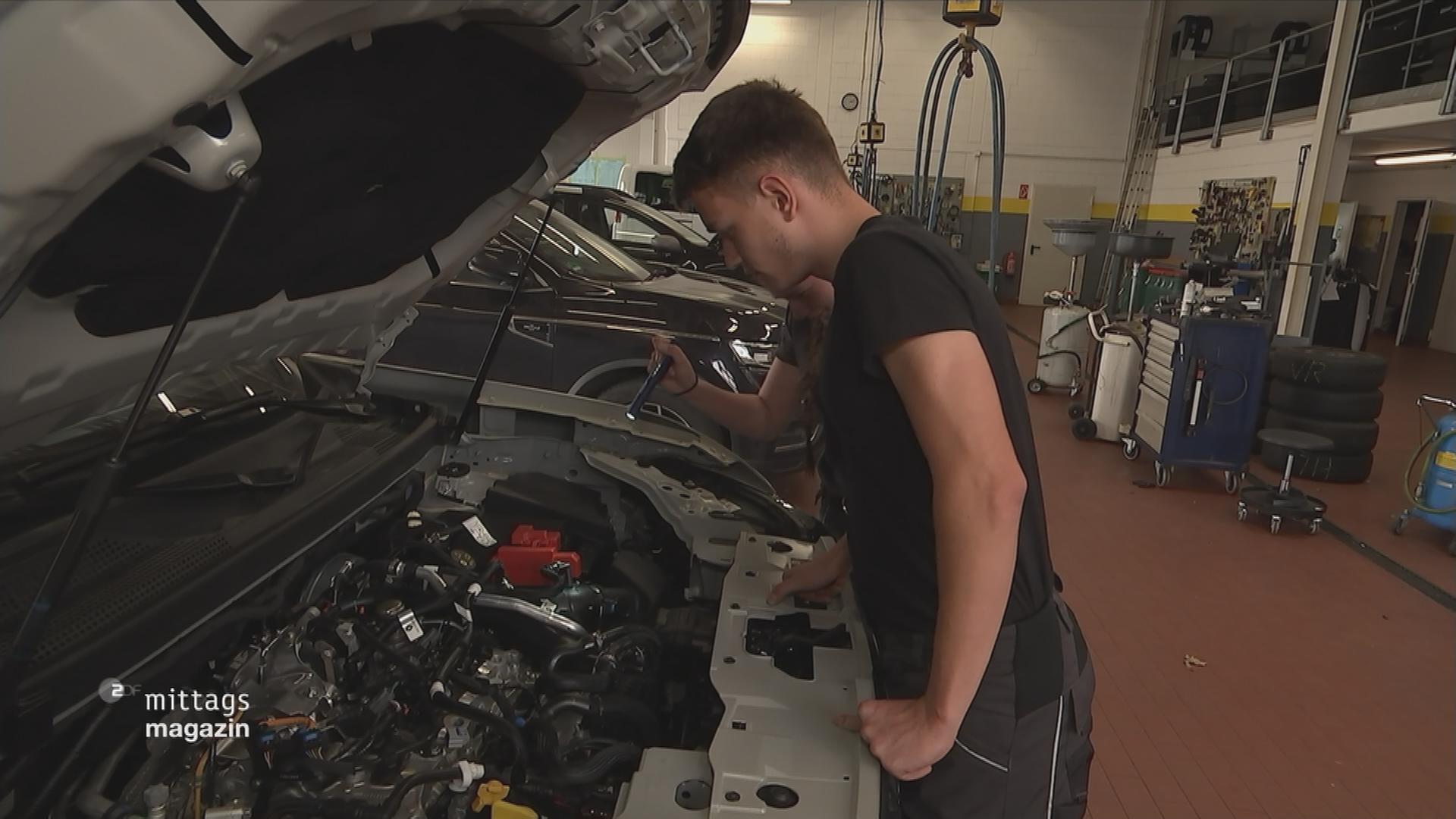 Azubi steht vor geöffnetem Motor eines Autos