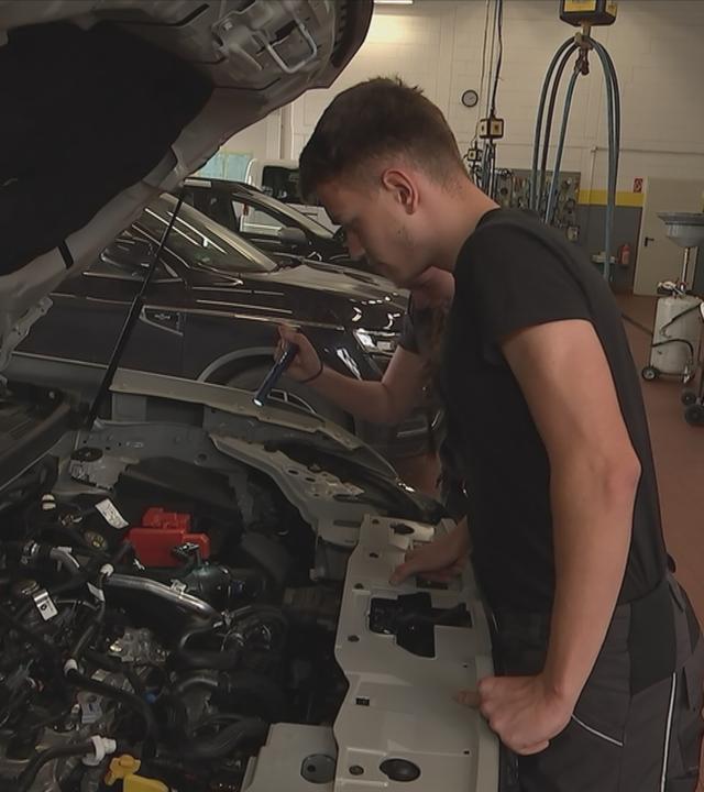 Azubi steht vor geöffnetem Motor eines Autos