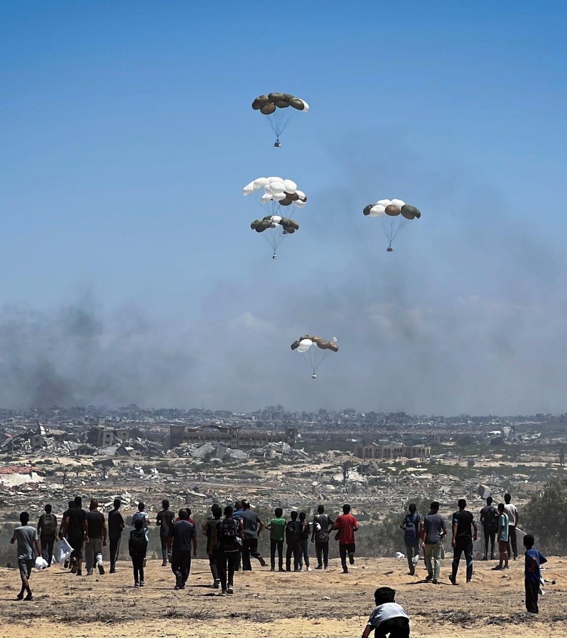Nusairat, Gazastreifen, Palästinensisches Gebiet: Palästinenser eilen zum Ort des Geschehens, als Luftpaletten mit humanitären Hilfsgütern über Nuseirat im zentralen Gazastreifen aus einem Militärflugzeug abgeworfen werden und mit Fallschirmen herabgleiten. Dies geschieht im Rahmen einer Luftabwurfmission über dem von Israel belagerten palästinensischen Gebiet am 5. August 2025.