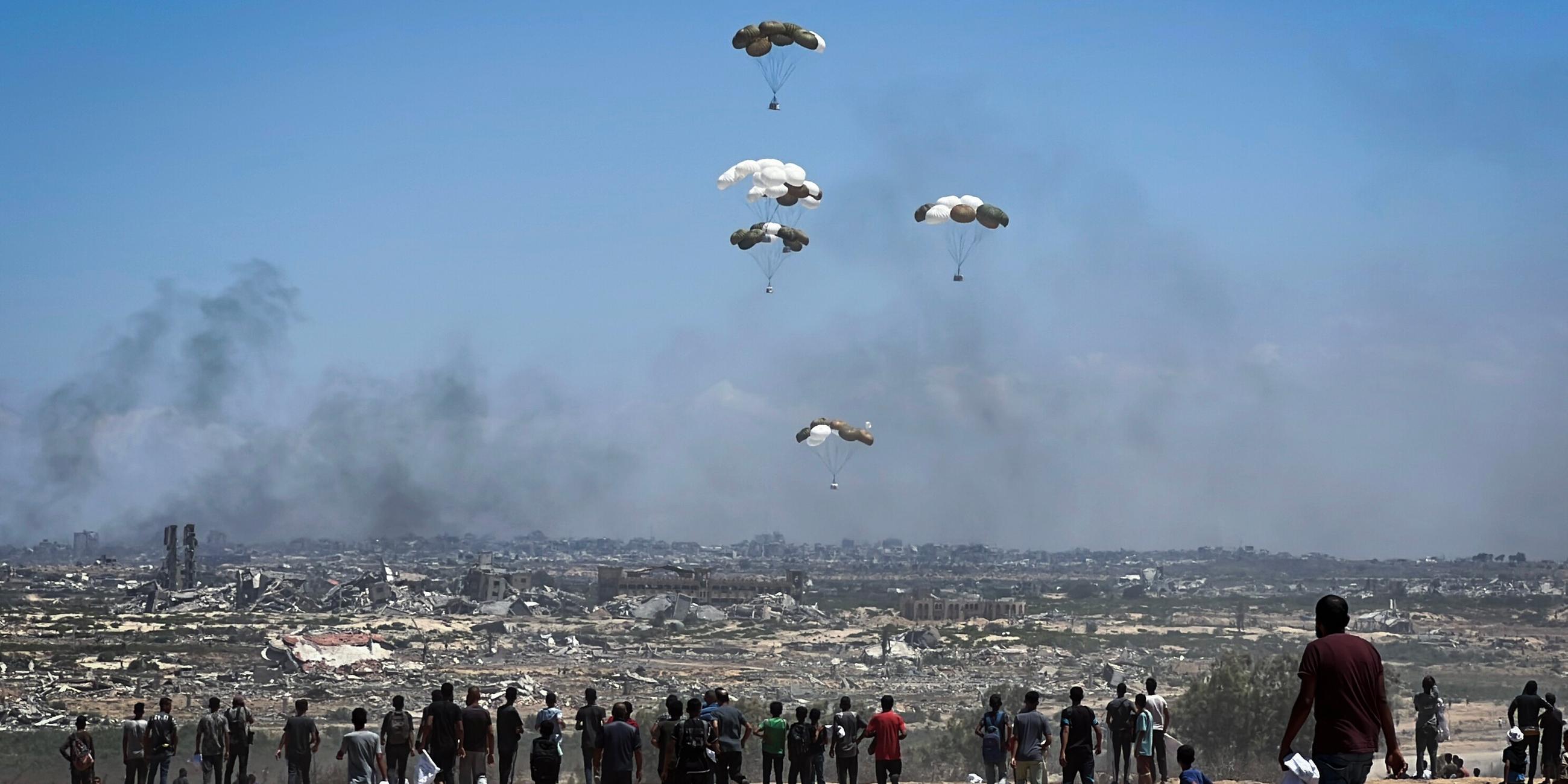 Nusairat, Gazastreifen, Palästinensisches Gebiet: Palästinenser eilen zum Ort des Geschehens, als Luftpaletten mit humanitären Hilfsgütern über Nuseirat im zentralen Gazastreifen aus einem Militärflugzeug abgeworfen werden und mit Fallschirmen herabgleiten. Dies geschieht im Rahmen einer Luftabwurfmission über dem von Israel belagerten palästinensischen Gebiet am 5. August 2025.