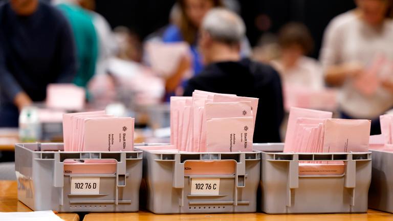 Briefwahlunterlagen zur Kommunalwahl in NRW liegen im Briefwahlzentrum Köln auf Tischen in Kisten. Bei der Auszählung der Briefwahlstimmen im Briefwahlzentrum in der Koelnmesse werden die roten Wahlbriefe von ehrenamtlichen Wahlhelfern auf ihre Gültigkeit überprüft.