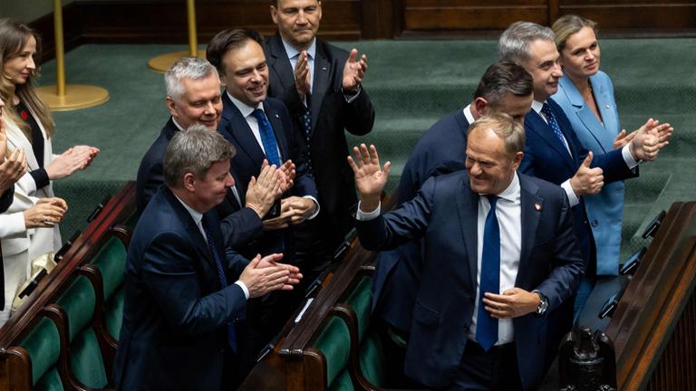 Donald Tusk winkt, umstehende Abgeordnete applaudieren