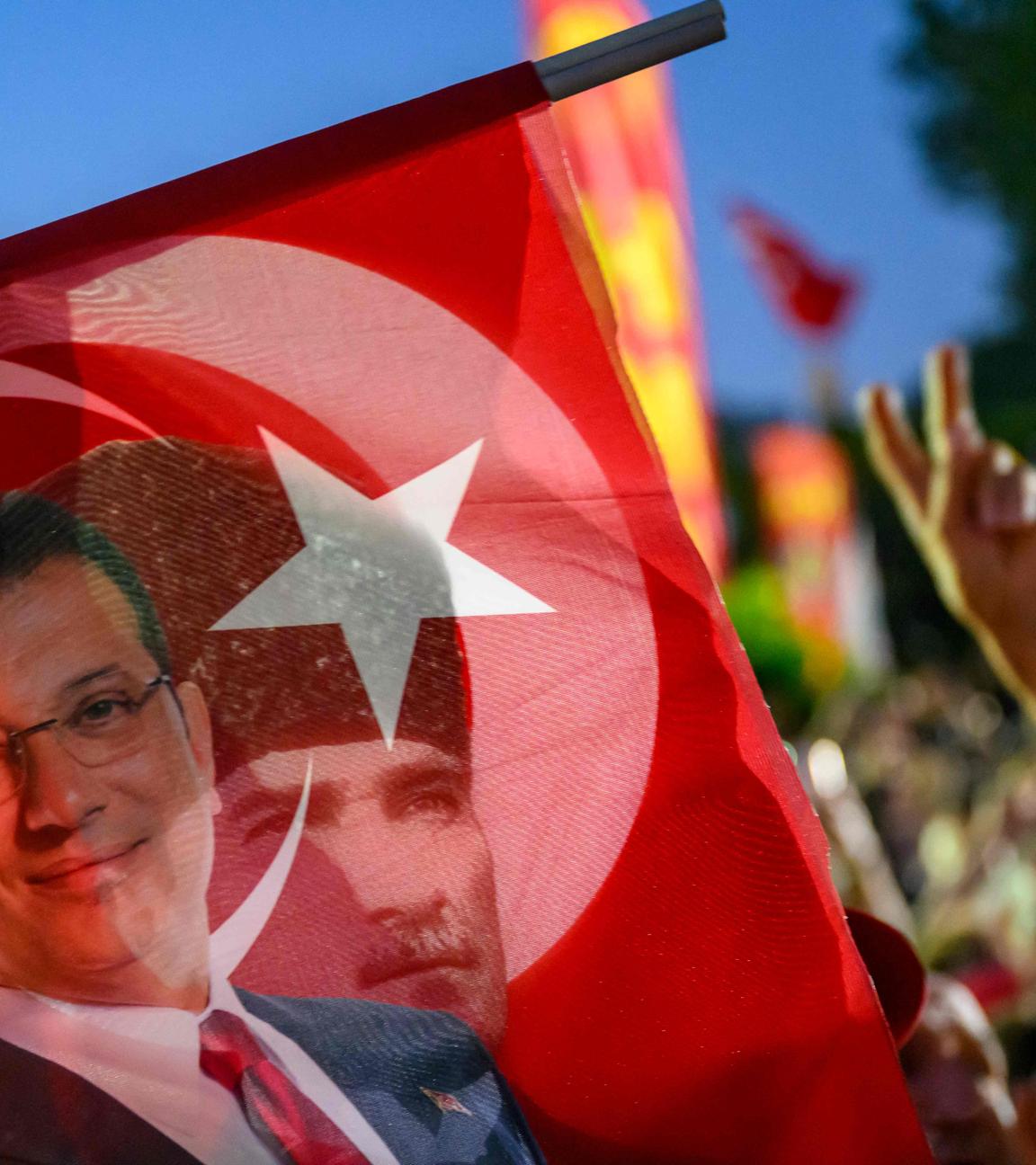 TOPSHOT - A supporter holds a flag of Istanbul's detained Mayor Ekrem Imamoglu and the First President of the Republic of Turkey Mustafa Kemal Ataturk as they listen to the leader of Turkey's main opposition Republican People's Party (CHP) Ozgur Ozel (not pictured) during a rally protesting the 100th day of the detention of Istanbul's Mayor, in Sarachane Square, Istanbul on July 1, 2025. (Photo by Yasin AKGUL / AFP)