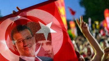 TOPSHOT - A supporter holds a flag of Istanbul's detained Mayor Ekrem Imamoglu and the First President of the Republic of Turkey Mustafa Kemal Ataturk as they listen to the leader of Turkey's main opposition Republican People's Party (CHP) Ozgur Ozel (not pictured) during a rally protesting the 100th day of the detention of Istanbul's Mayor, in Sarachane Square, Istanbul on July 1, 2025. (Photo by Yasin AKGUL / AFP)