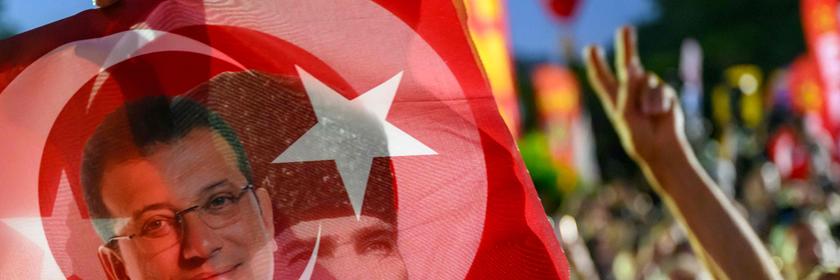 TOPSHOT - A supporter holds a flag of Istanbul's detained Mayor Ekrem Imamoglu and the First President of the Republic of Turkey Mustafa Kemal Ataturk as they listen to the leader of Turkey's main opposition Republican People's Party (CHP) Ozgur Ozel (not pictured) during a rally protesting the 100th day of the detention of Istanbul's Mayor, in Sarachane Square, Istanbul on July 1, 2025. (Photo by Yasin AKGUL / AFP)