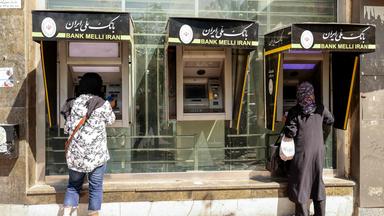 Menschen heben am 28. September 2025 in der iranischen Hauptstadt Teheran Geld an einem Geldautomaten ab.