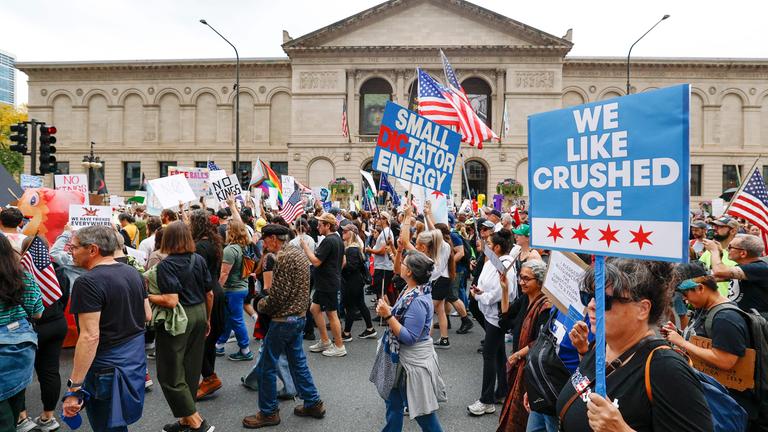 Es sind Menschen zu sehen, die verscheidene Plakate während einer Kundgebung des nationalen Protesttages No Kings hochhalten.