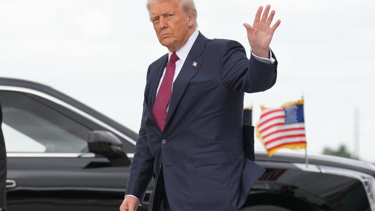 Trump ist zu sehen, während er winkend in die Kamera blickt